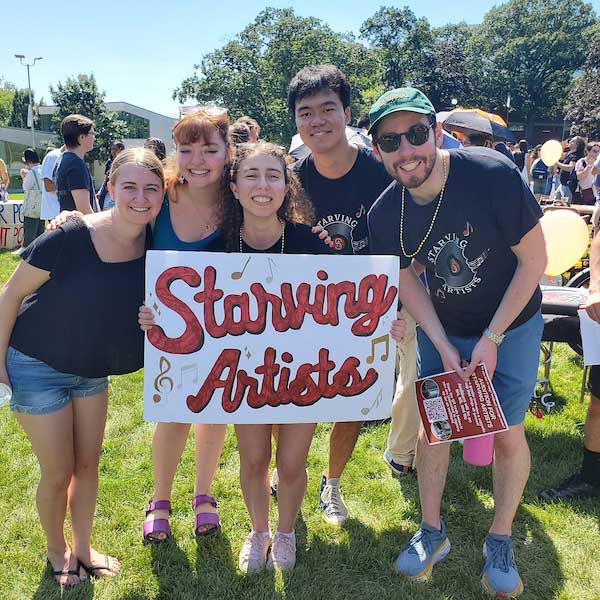 A group of students pose together for a photo and hold up a sign that reads: "Starving Artists"