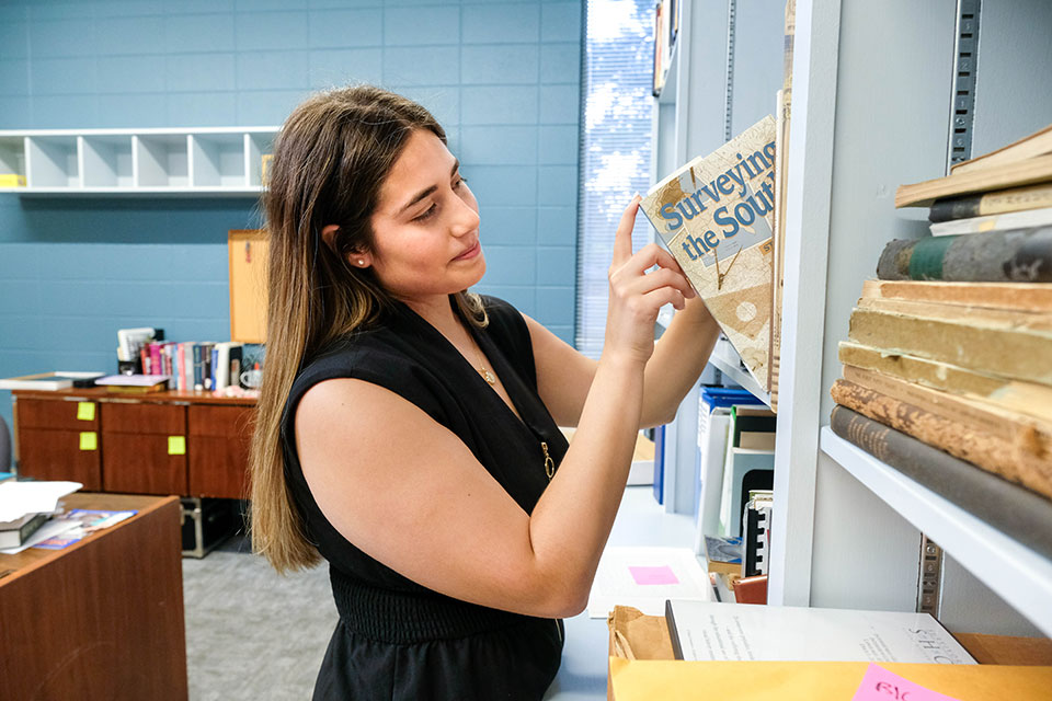 Lauren Balfour pulls a book off of a bookshelf.
