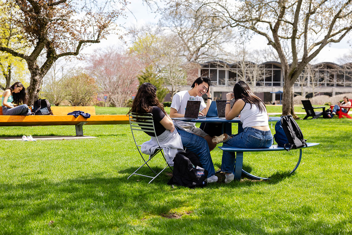 Students sit outside together at a table on a sunny day.