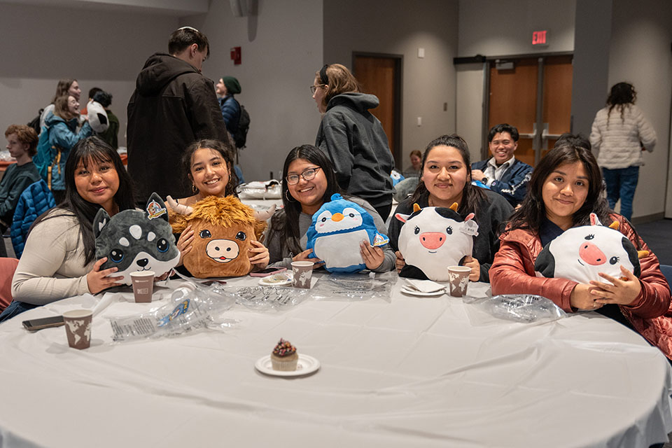Five students sit at a table showing off the squishmallows they just created at the event.