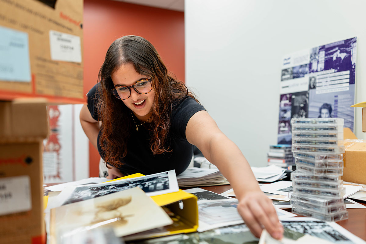 A student reaches for a document over a table covered in photographs and documents.