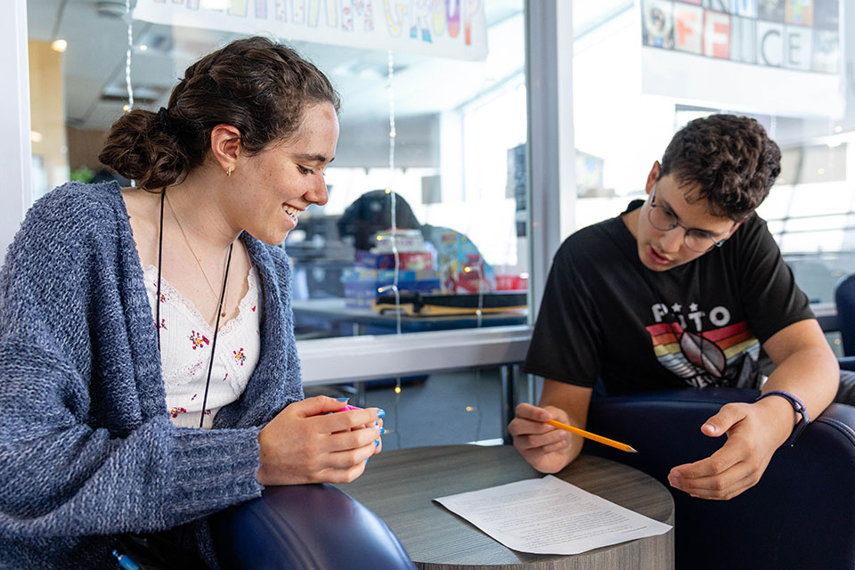 A Genesis program student sits at a table with an instructor a discusses a paper.