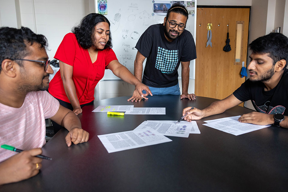 A group of graduate students discuss documents around a table.