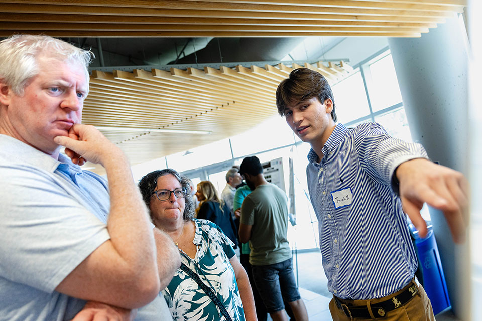 Hillemann speaks to two people and points to his research poster.