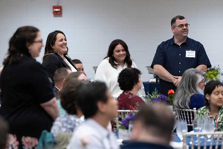 Four staff members stand next to table at staff recognition lunch.