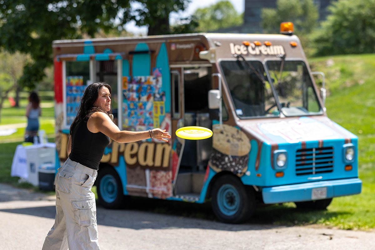 A person throws a frisbee in front of an ice cream truck outside on the Brandeis campus.
