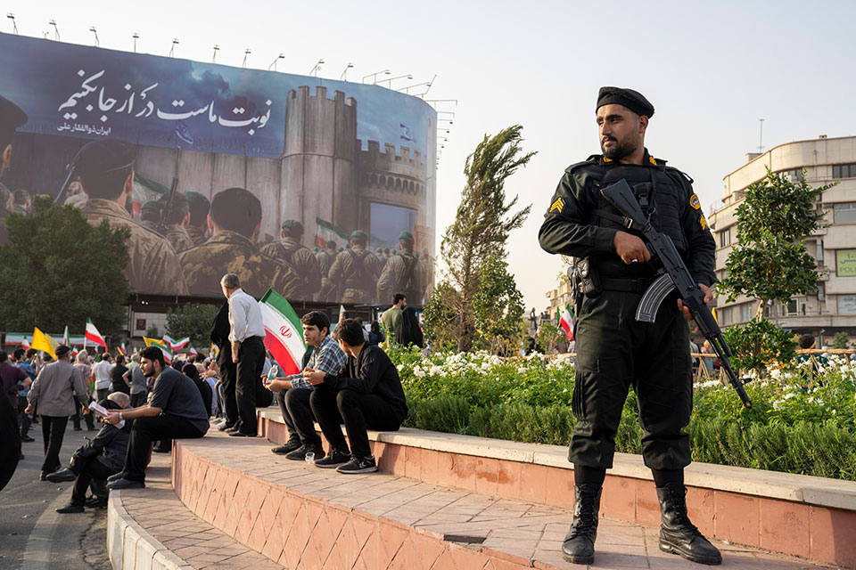 A police officer stands guard as demonstrators wave flags and cheer during a gathering to honor Iran’s military forces.