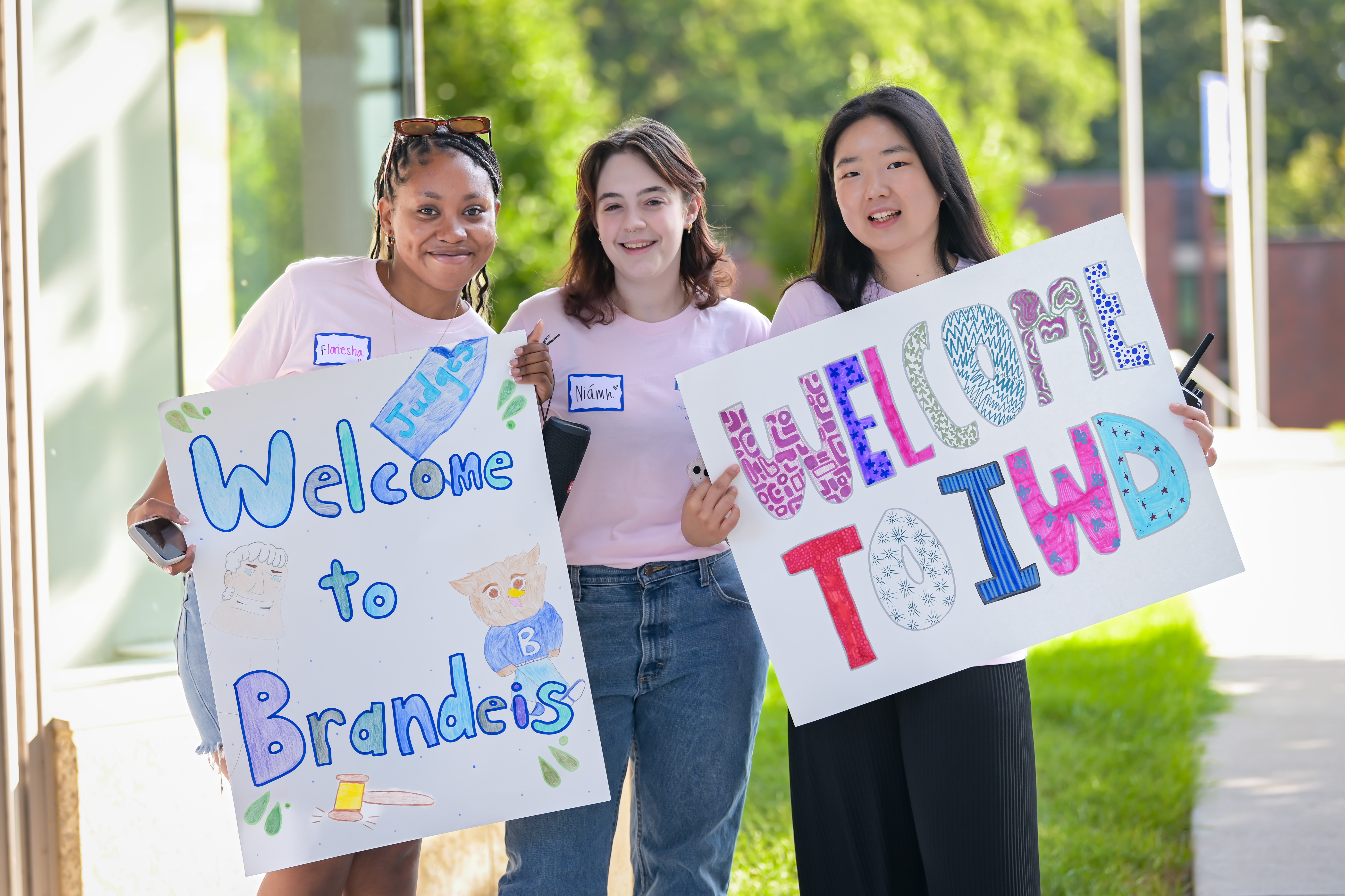 Three students holding a post that says welcome to brandeis