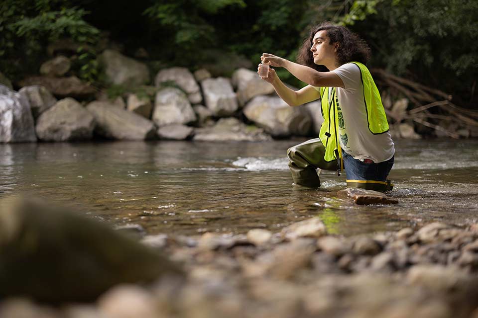 Lucas kneeling in a river collecting a water sample.