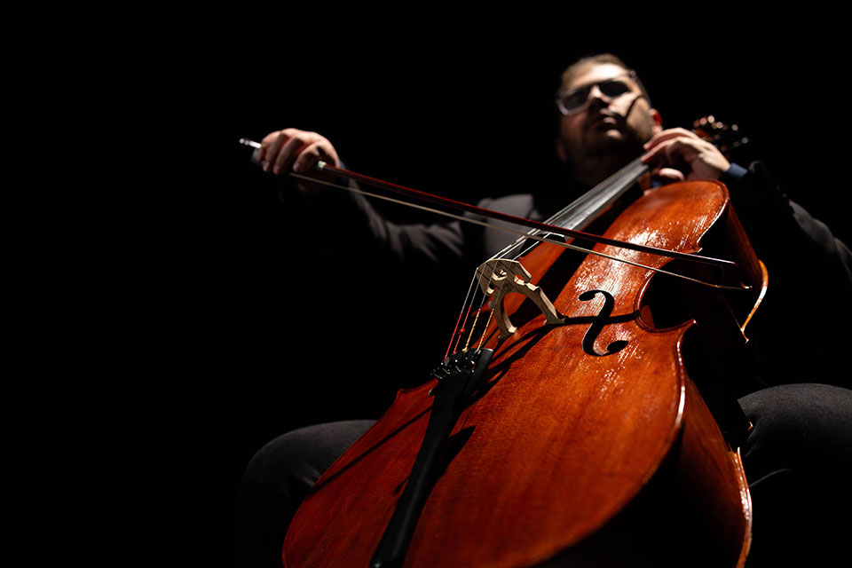 Person playing a cello on a dark stage