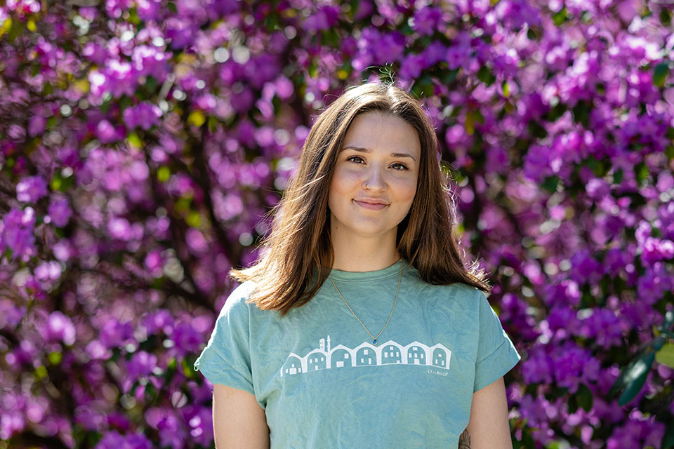 Hana Klempnauer Miller stands in front of a purple flowering bush