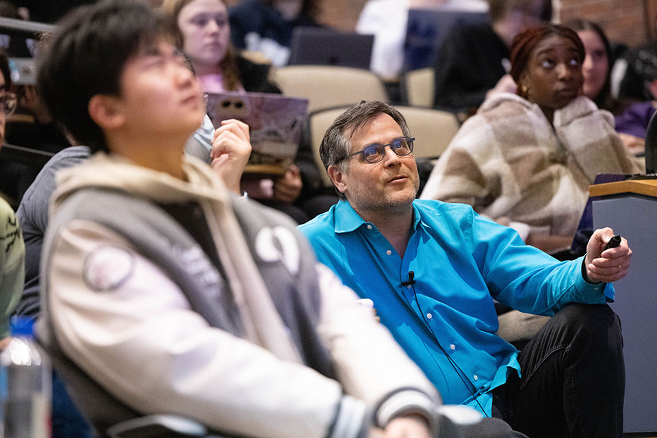 A professor and students look up toward a presentation in a lecture hall
