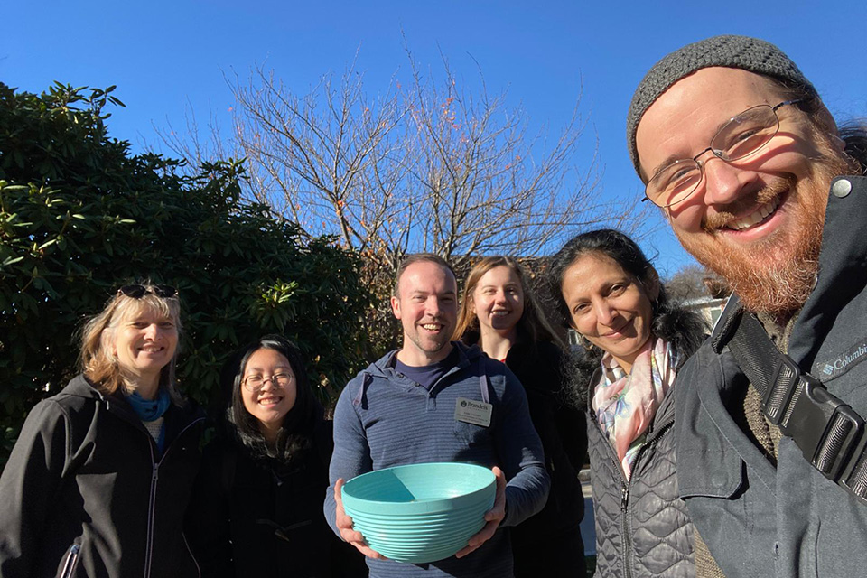 a small group of people, one holding a big blue bowl, standing outside and smiling at camera