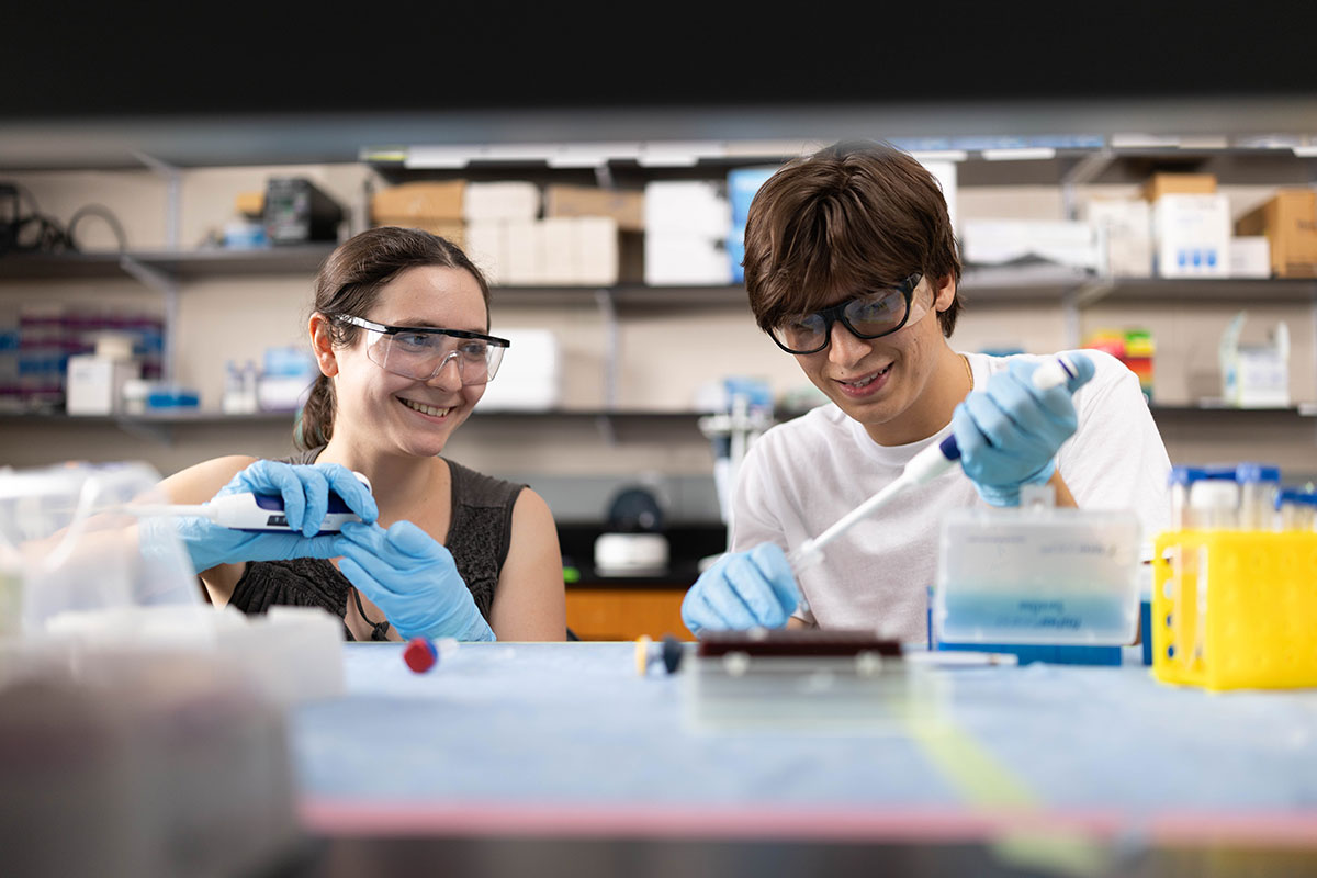 Two students use pipettes in a lab.