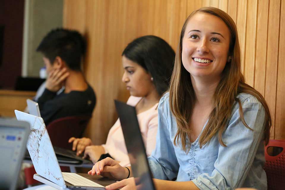 Smiling student sitting at a laptop in a classroom