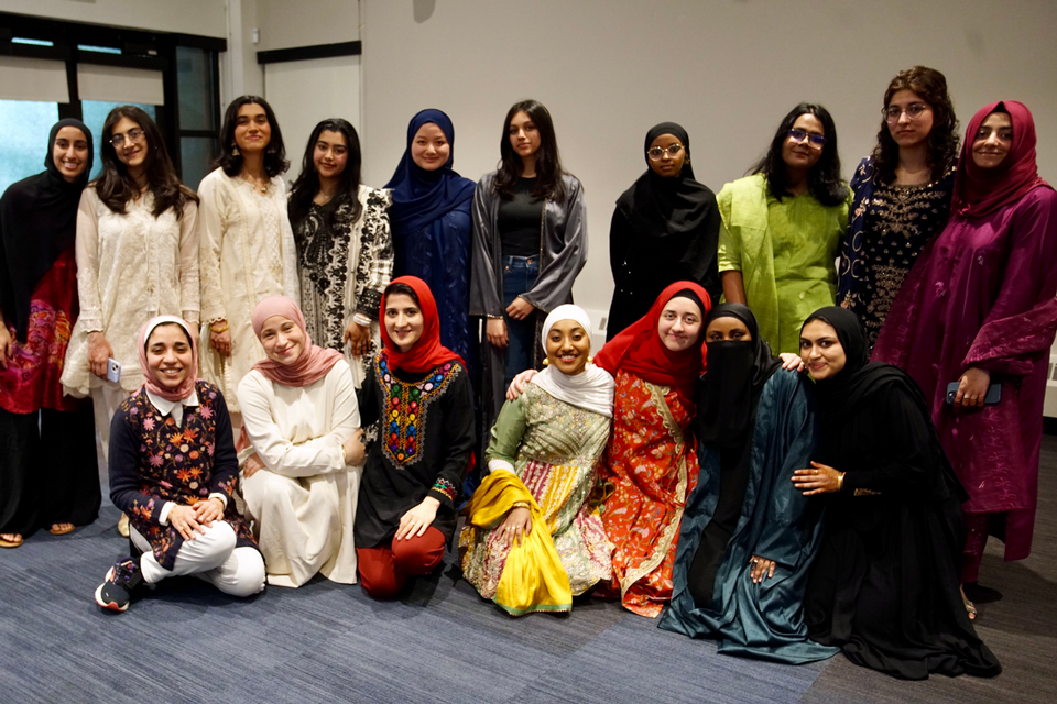 a group of many women in colorful clothes and hijabs standing and kneeling in a room and smiling into the camera